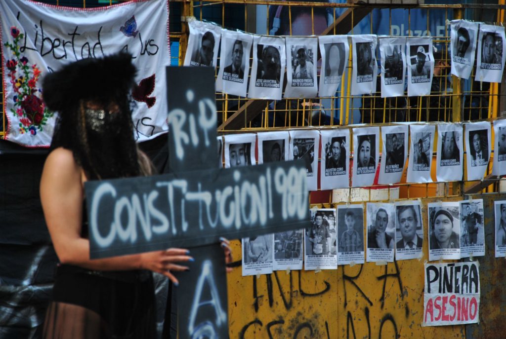 Mujer sujetando una cruz frente a fotografías de personas muertas o heridas luego del estallido social en chile para el 18 de octubre