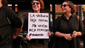 Mujer con cartel en marcha feminsita que dice "La violencia deja marcas, no verlas deja femicidios #niunamenos"