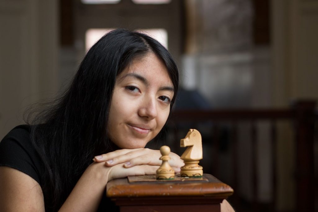 Javiera Gómez apoyada en una baranda con piezas de ajedrez mirando a la cámara